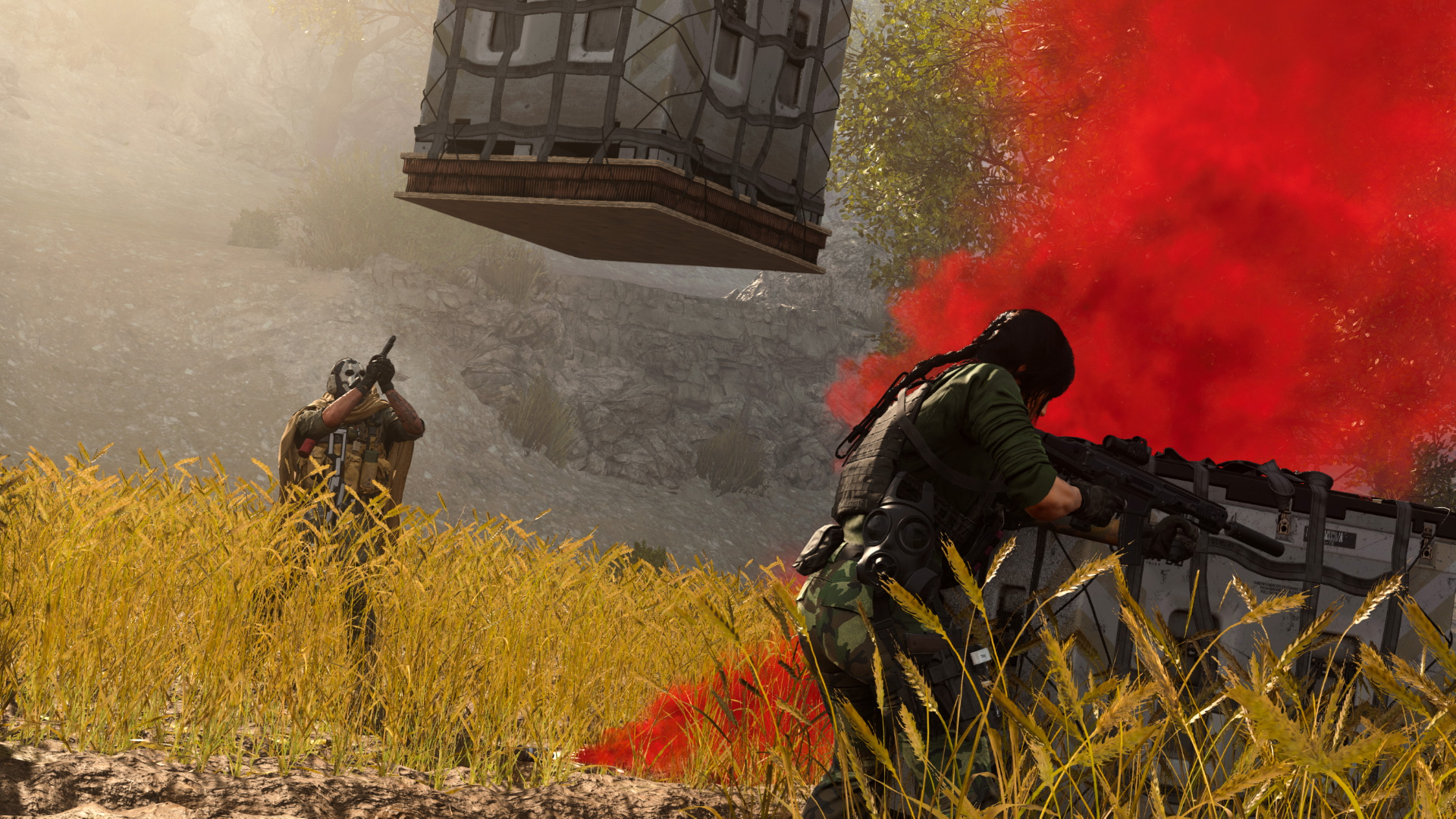 Two soldiers are positioned in a field, their rifles held high, beside a billowing column of red smoke. On the ground, a supply crate is present, while another is in the process of being lowered to their location.