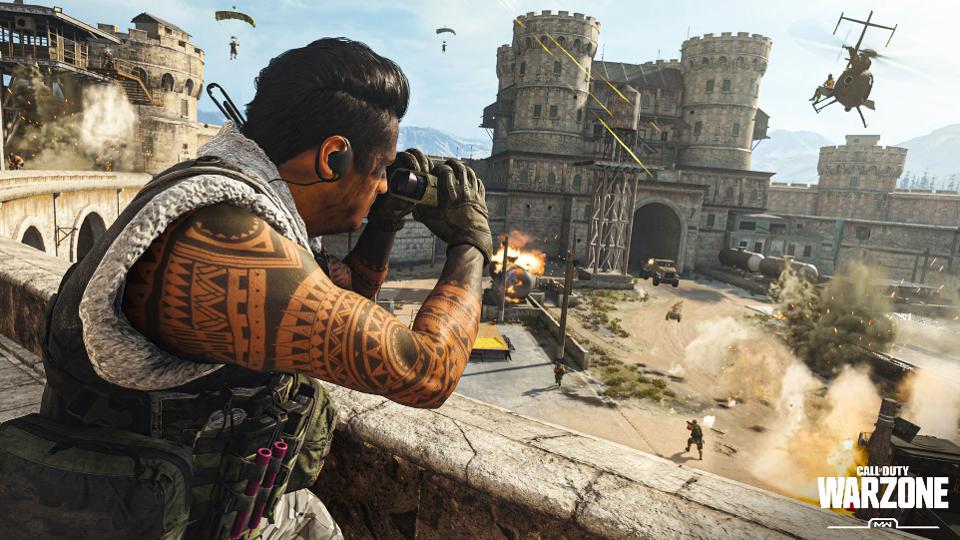 A soldier adorned with numerous tattoos peers through binoculars over a barrier, observing the chaos of battle unfolding beneath him, complete with gunfire and a helicopter, all set against the backdrop of a castle.