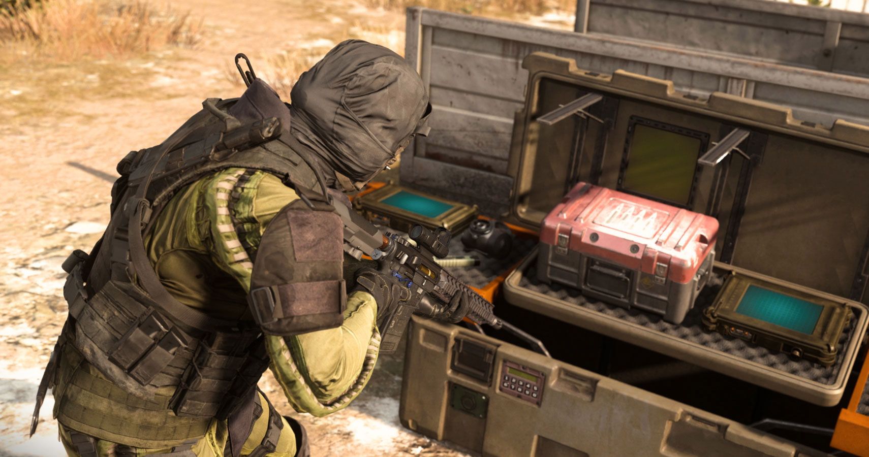 A soldier kneels beside an open supply crate, which contains a red box and two devices featuring screens.